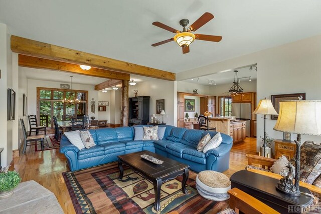 living room with ceiling fan with notable chandelier, beamed ceiling, and light hardwood / wood-style flooring