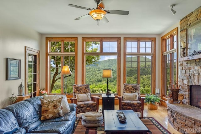 sunroom with ceiling fan and a stone fireplace