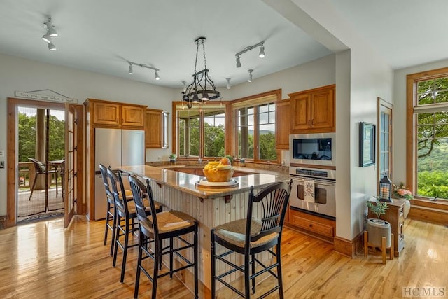 kitchen with stainless steel appliances, a center island, light stone countertops, decorative light fixtures, and light wood-type flooring