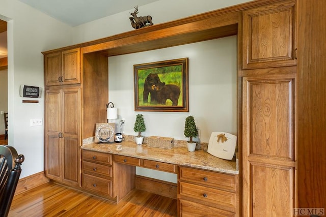 interior space with light wood-type flooring, built in desk, and light stone counters