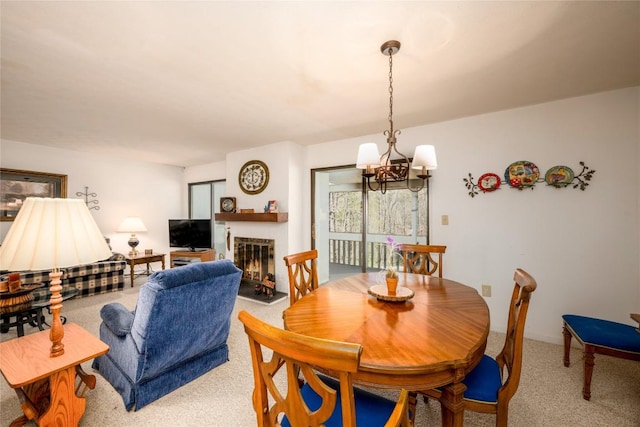 dining space with light colored carpet, a notable chandelier, and a warm lit fireplace