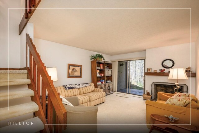 carpeted living area with a large fireplace and stairs