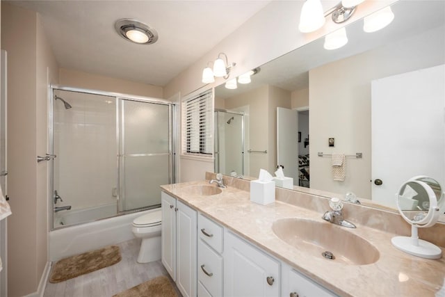bathroom with bath / shower combo with glass door, toilet, double vanity, and a sink