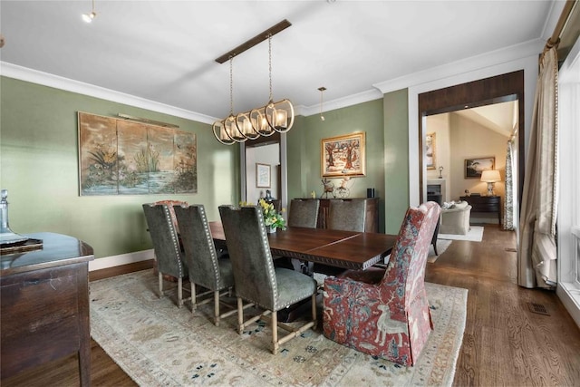 dining room featuring wood finished floors, crown molding, visible vents, and baseboards