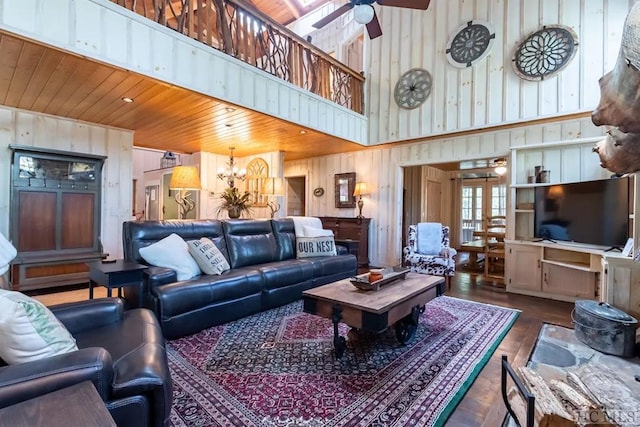 living room with a high ceiling, ceiling fan with notable chandelier, wood walls, wooden ceiling, and dark hardwood / wood-style flooring