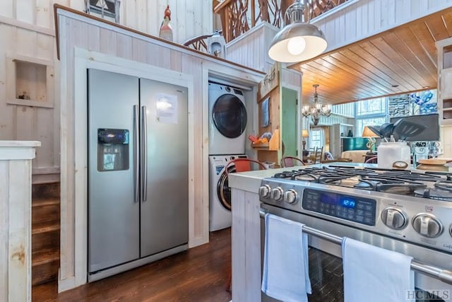 kitchen featuring stacked washer / dryer, stainless steel appliances, an inviting chandelier, dark hardwood / wood-style floors, and wood walls