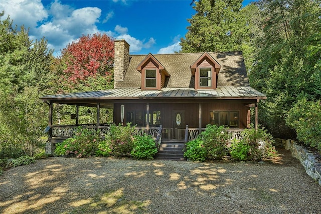 view of front of house featuring a porch, a standing seam roof, metal roof, and a chimney