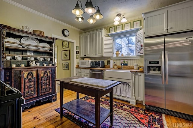 kitchen with pendant lighting, appliances with stainless steel finishes, a notable chandelier, ornamental molding, and light hardwood / wood-style floors