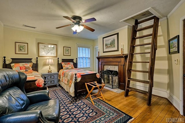 bedroom with ceiling fan, ornamental molding, a tile fireplace, and wood-type flooring