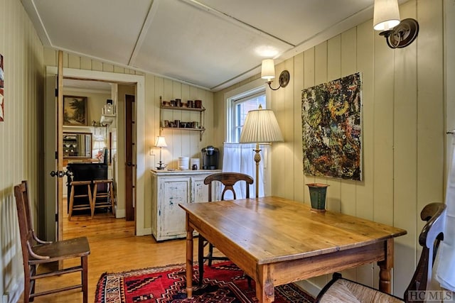 dining space with ornamental molding, light hardwood / wood-style floors, and wood walls