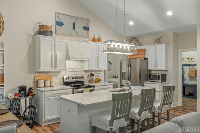 kitchen with sink, appliances with stainless steel finishes, white cabinetry, hanging light fixtures, and custom range hood