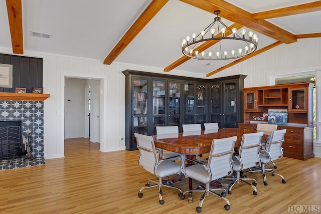 dining area with a tiled fireplace, vaulted ceiling with beams, a chandelier, and light hardwood / wood-style flooring