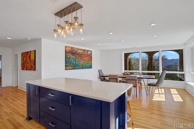 kitchen featuring light hardwood / wood-style flooring, hanging light fixtures, a kitchen breakfast bar, blue cabinetry, and a center island