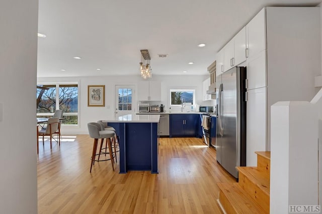 kitchen with decorative light fixtures, blue cabinets, appliances with stainless steel finishes, white cabinets, and a breakfast bar area