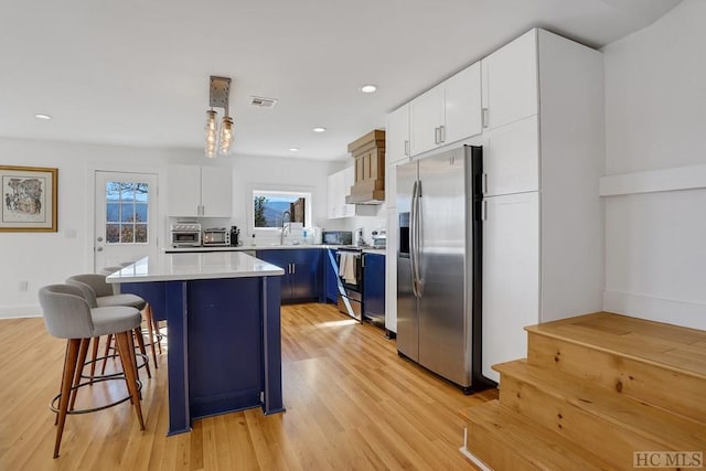 kitchen featuring white cabinetry, a kitchen island, blue cabinets, appliances with stainless steel finishes, and a kitchen breakfast bar