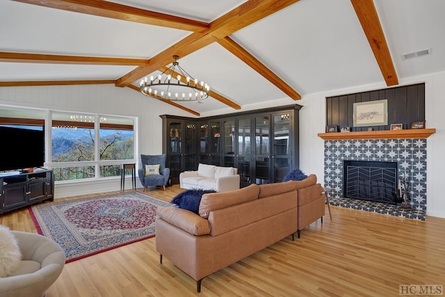 living room with light hardwood / wood-style floors, a chandelier, vaulted ceiling with beams, and a tiled fireplace