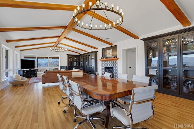 dining room with light wood-type flooring, lofted ceiling with beams, a notable chandelier, and a fireplace