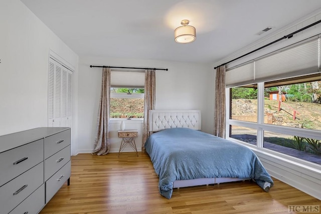 bedroom with light wood-type flooring, multiple windows, and a closet