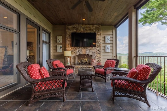 sunroom / solarium featuring ceiling fan, wooden ceiling, and an outdoor stone fireplace