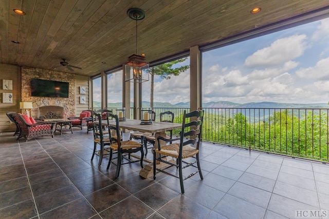 sunroom with ceiling fan, wood ceiling, an outdoor stone fireplace, and a water view