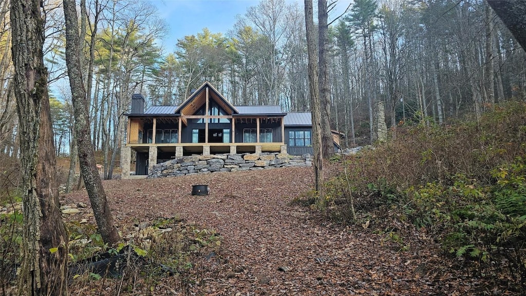 back of property featuring a forest view, a standing seam roof, a sunroom, a chimney, and metal roof