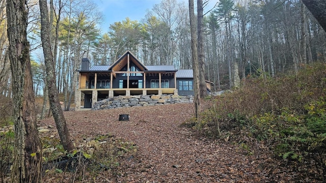 back of property featuring a forest view, a standing seam roof, a sunroom, a chimney, and metal roof