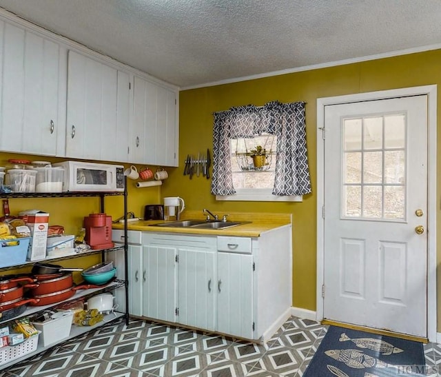 kitchen with crown molding, white cabinetry, sink, and a textured ceiling