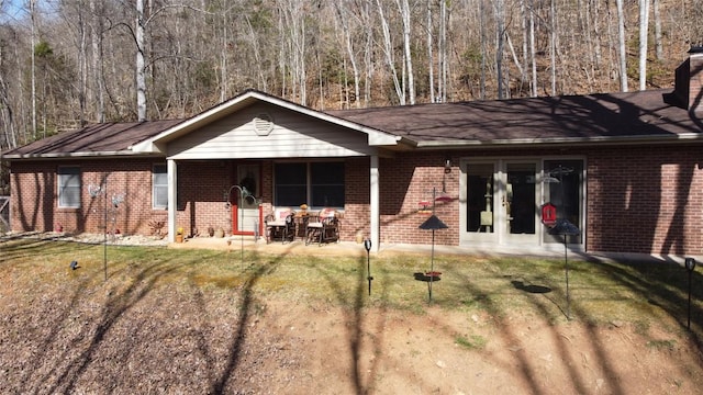 ranch-style home with french doors, brick siding, a patio area, a wooded view, and a front lawn