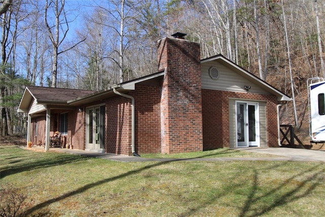 view of home's exterior with french doors, brick siding, a lawn, and a chimney