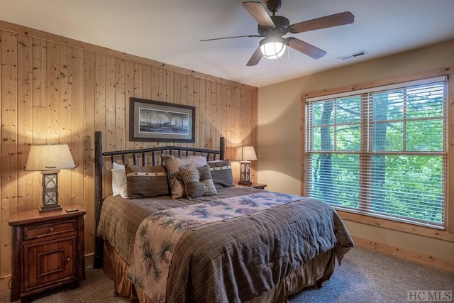 carpeted bedroom with ceiling fan, multiple windows, and wood walls