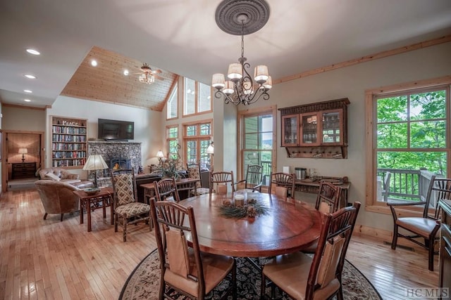 dining room with wood ceiling, a fireplace, a notable chandelier, light wood-type flooring, and high vaulted ceiling