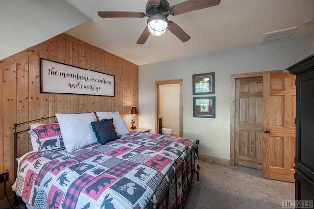 bedroom featuring carpet, wooden walls, connected bathroom, and ceiling fan