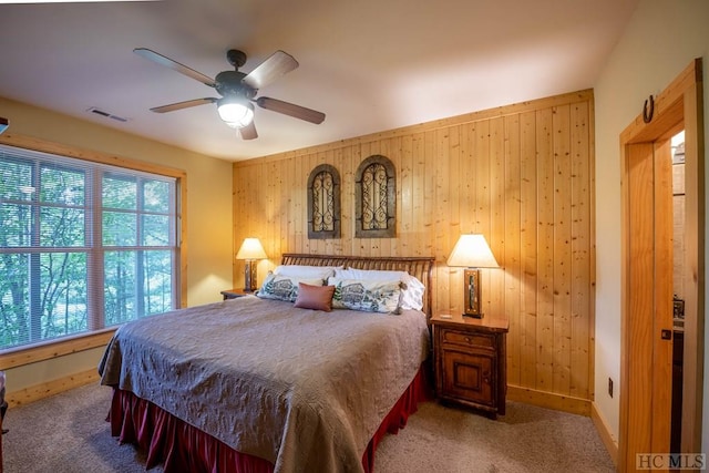 carpeted bedroom featuring wood walls and ceiling fan