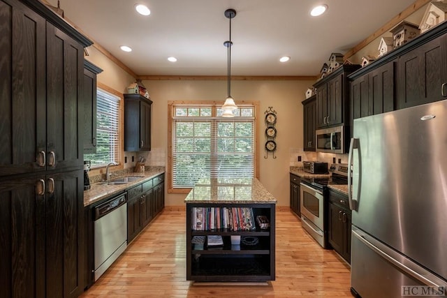 kitchen featuring appliances with stainless steel finishes, a center island, decorative light fixtures, ornamental molding, and light stone counters