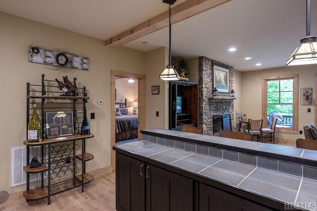 kitchen featuring light wood-type flooring, beam ceiling, tile counters, and pendant lighting