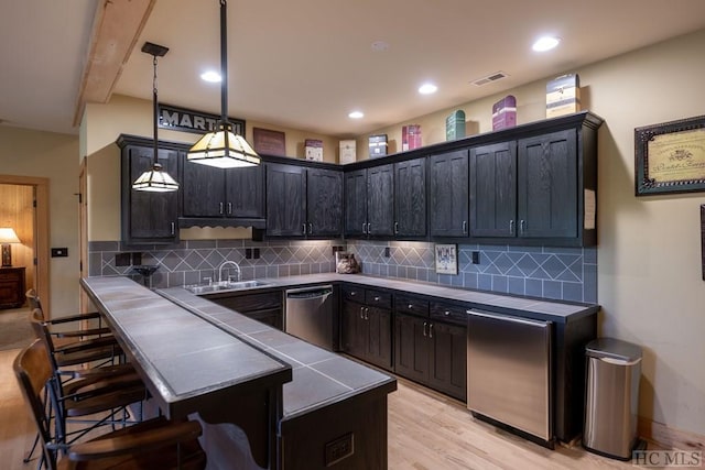 kitchen with pendant lighting, a kitchen breakfast bar, backsplash, sink, and stainless steel dishwasher