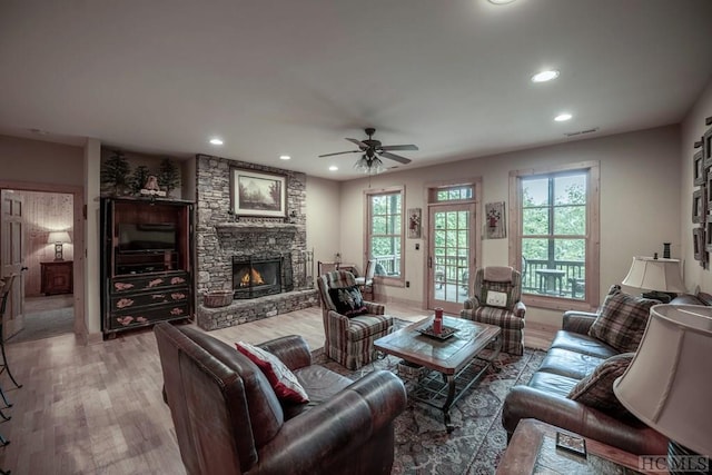 living room with hardwood / wood-style flooring, a stone fireplace, and ceiling fan