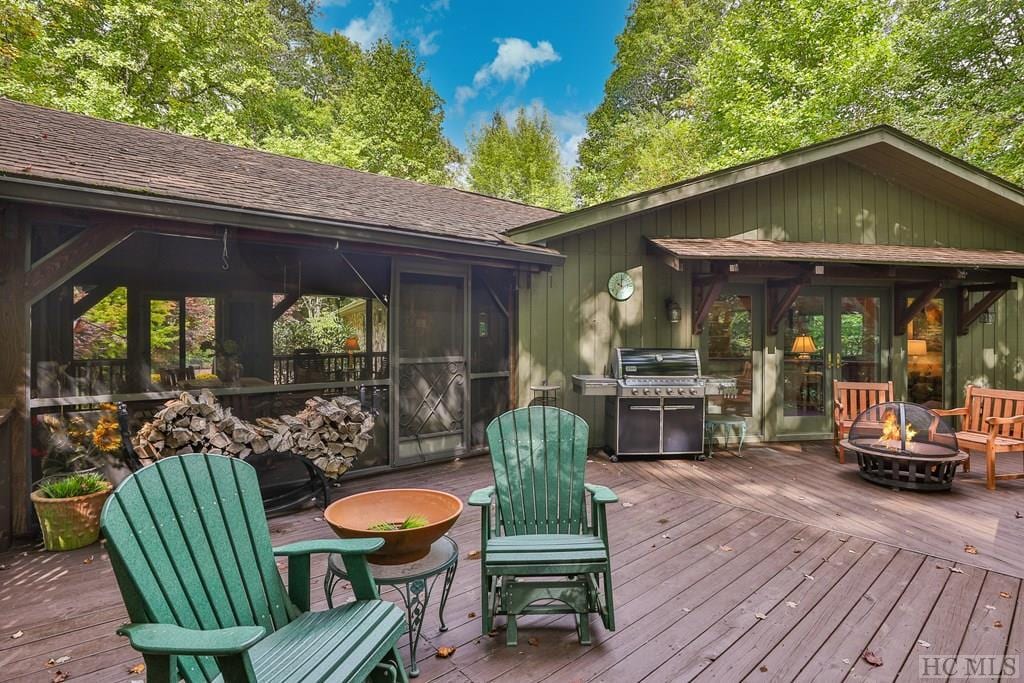 wooden deck with area for grilling, a sunroom, and a fire pit