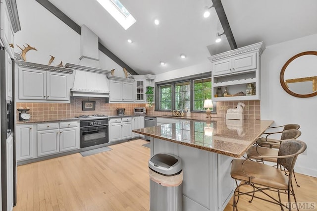 kitchen with a kitchen bar, dark stone counters, a skylight, stainless steel appliances, and kitchen peninsula