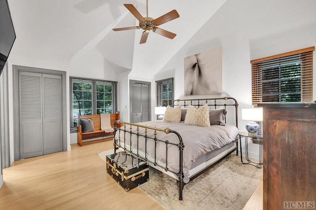 bedroom with ceiling fan, two closets, light wood-type flooring, and high vaulted ceiling