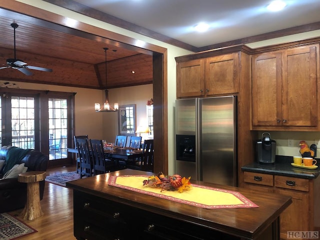 kitchen featuring hardwood / wood-style flooring, stainless steel fridge, ceiling fan with notable chandelier, a center island, and decorative light fixtures