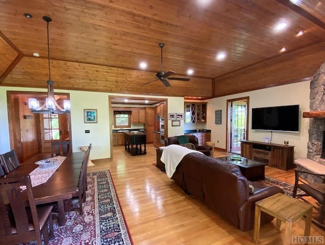 living room featuring lofted ceiling, a stone fireplace, wood ceiling, light wood-type flooring, and ceiling fan with notable chandelier