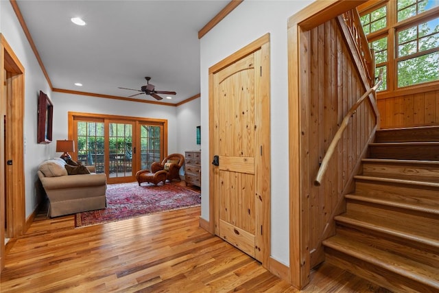 living area with ornamental molding, light wood-type flooring, stairs, plenty of natural light, and a ceiling fan