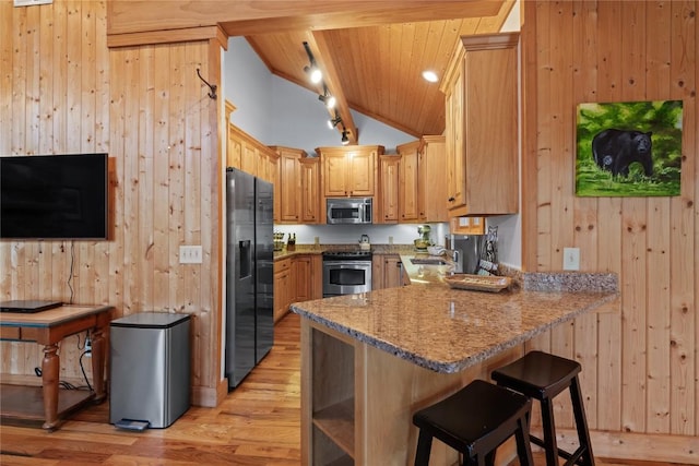 kitchen featuring appliances with stainless steel finishes, a peninsula, wood walls, light wood finished floors, and a kitchen bar