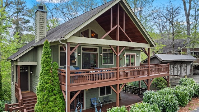 rear view of house featuring a shingled roof, a chimney, a deck, and board and batten siding
