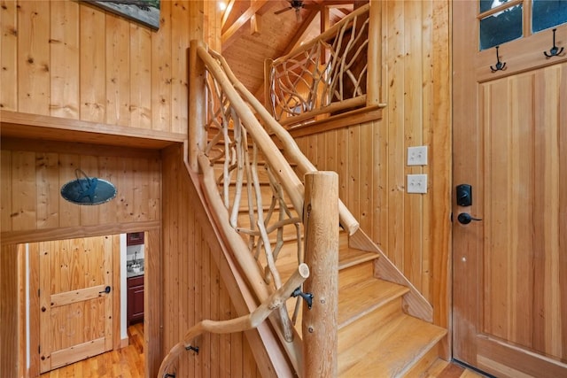 stairs with wooden walls, vaulted ceiling, wood finished floors, and ceiling fan