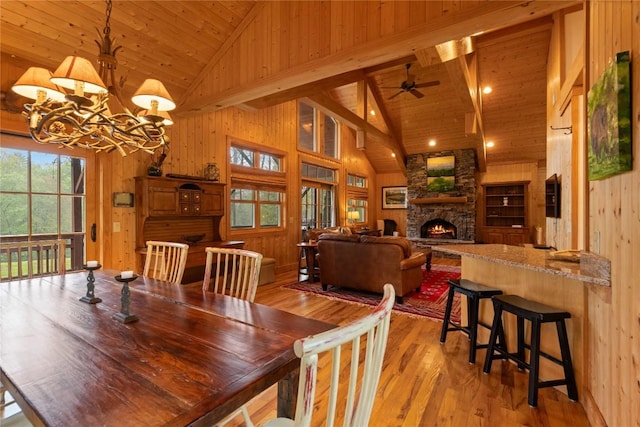dining area with wooden walls, a fireplace, light wood finished floors, high vaulted ceiling, and a chandelier