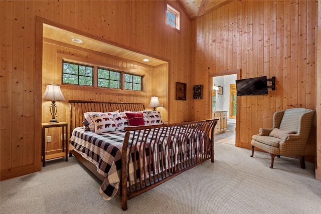 bedroom featuring light colored carpet, wooden walls, high vaulted ceiling, and connected bathroom