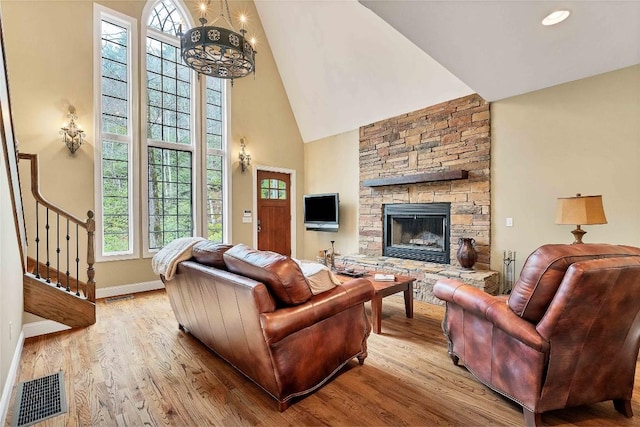 living room featuring high vaulted ceiling, visible vents, a stone fireplace, and light wood finished floors