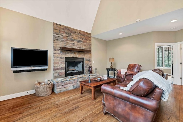 living area featuring light wood-style flooring, baseboards, vaulted ceiling, and a stone fireplace